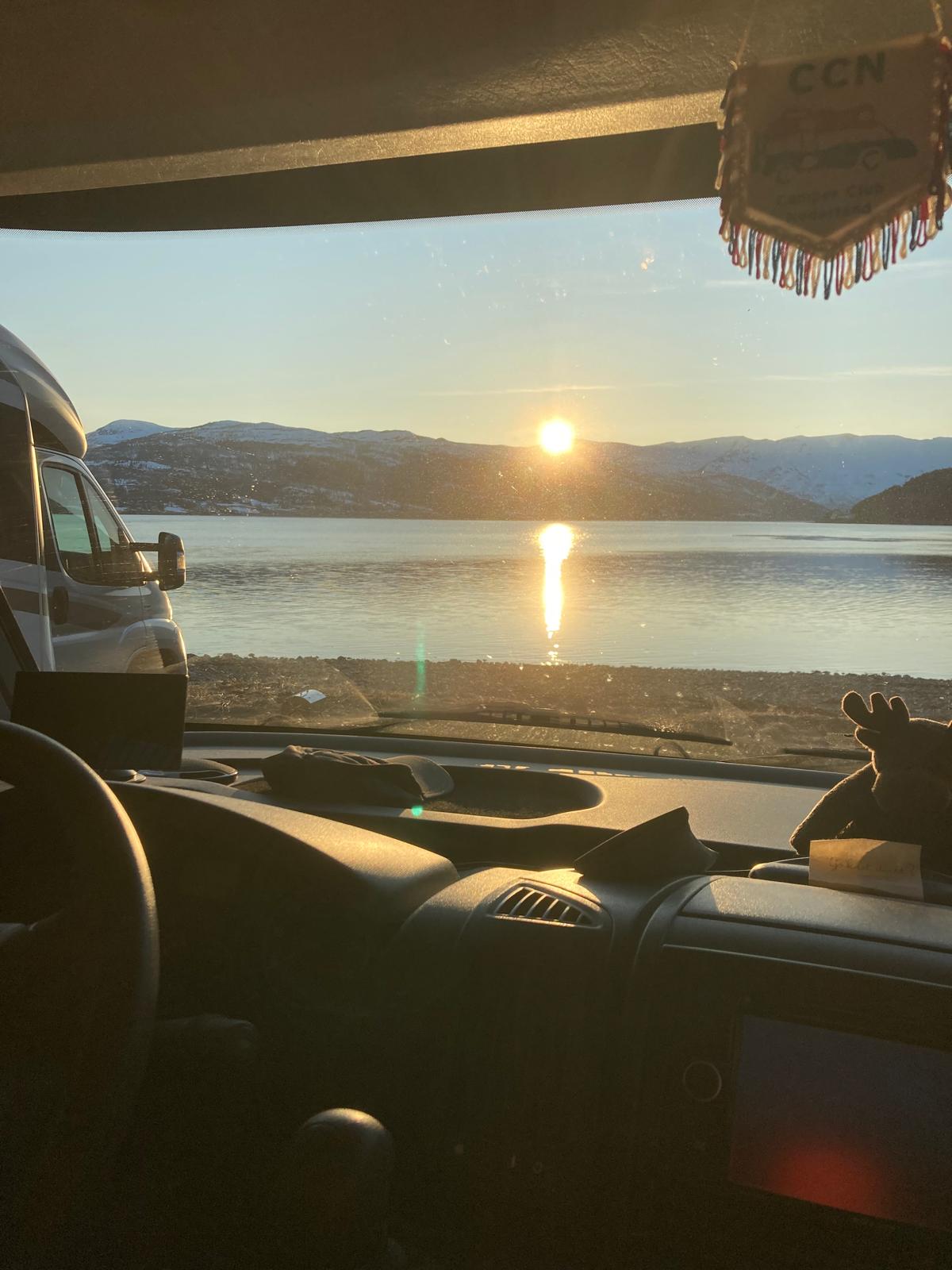 uitzicht vanuit camper bij zonsondergang aan meer met bergen